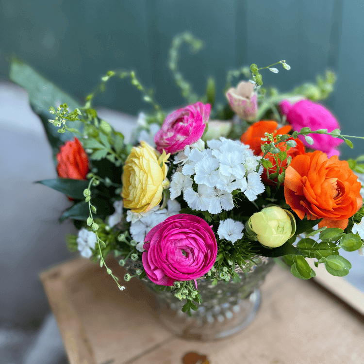 yellow,pink,and orange rannunculus with white dianthus in a crystal compote with a green background
